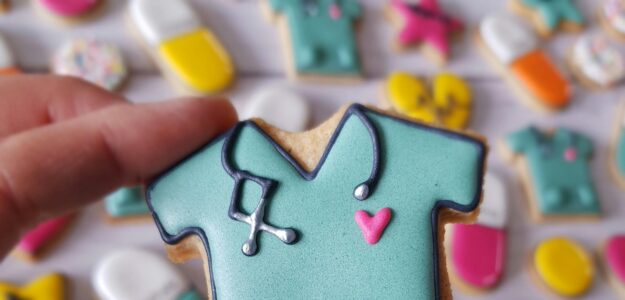 Close-up of a nurse-themed cookie with colorful desserts in the background.